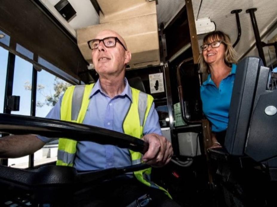 A man behind the wheel of a bus and a woman behind him smiling